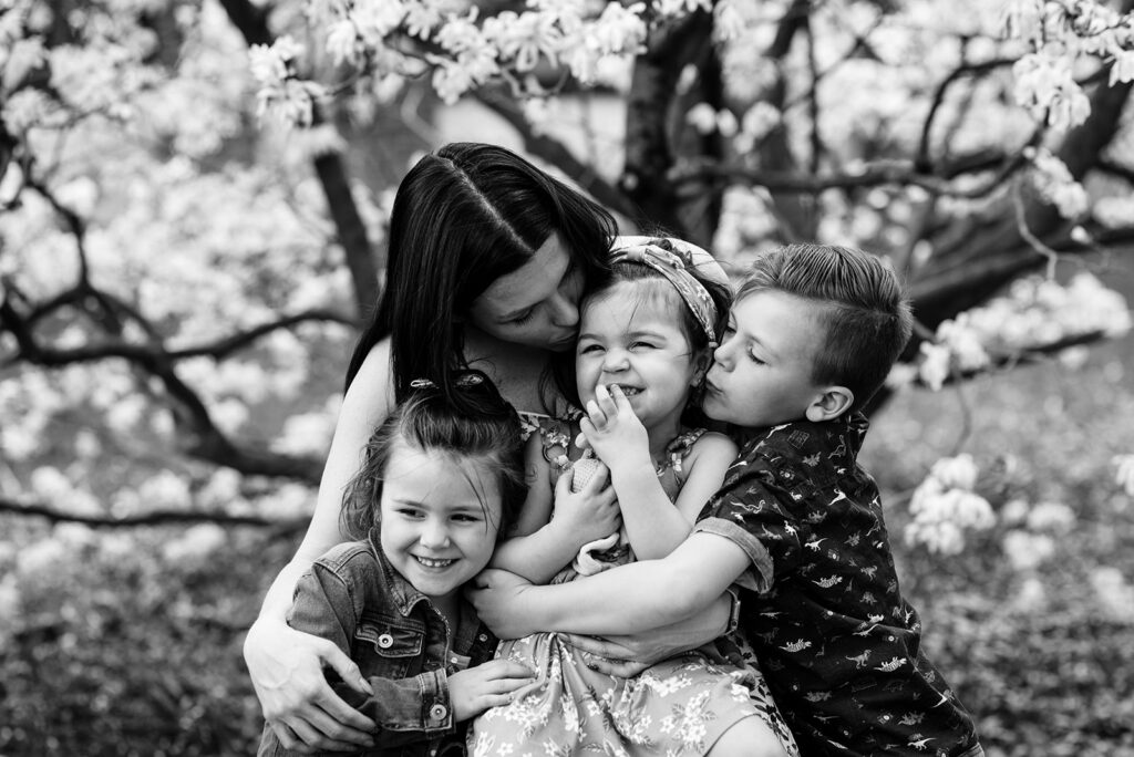 Captured in Time: A Mother's Love Shines Through - A black and white photograph of a mother and her three children huddled together. The mother tenderly kisses one of her children, while the others snuggle close, creating a heartwarming tableau of love and connection